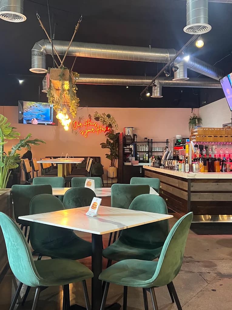 Dining room at Haven Haus Cafe with green velvet chairs, marble tables and a neon sign reading Our Haus is your Haus