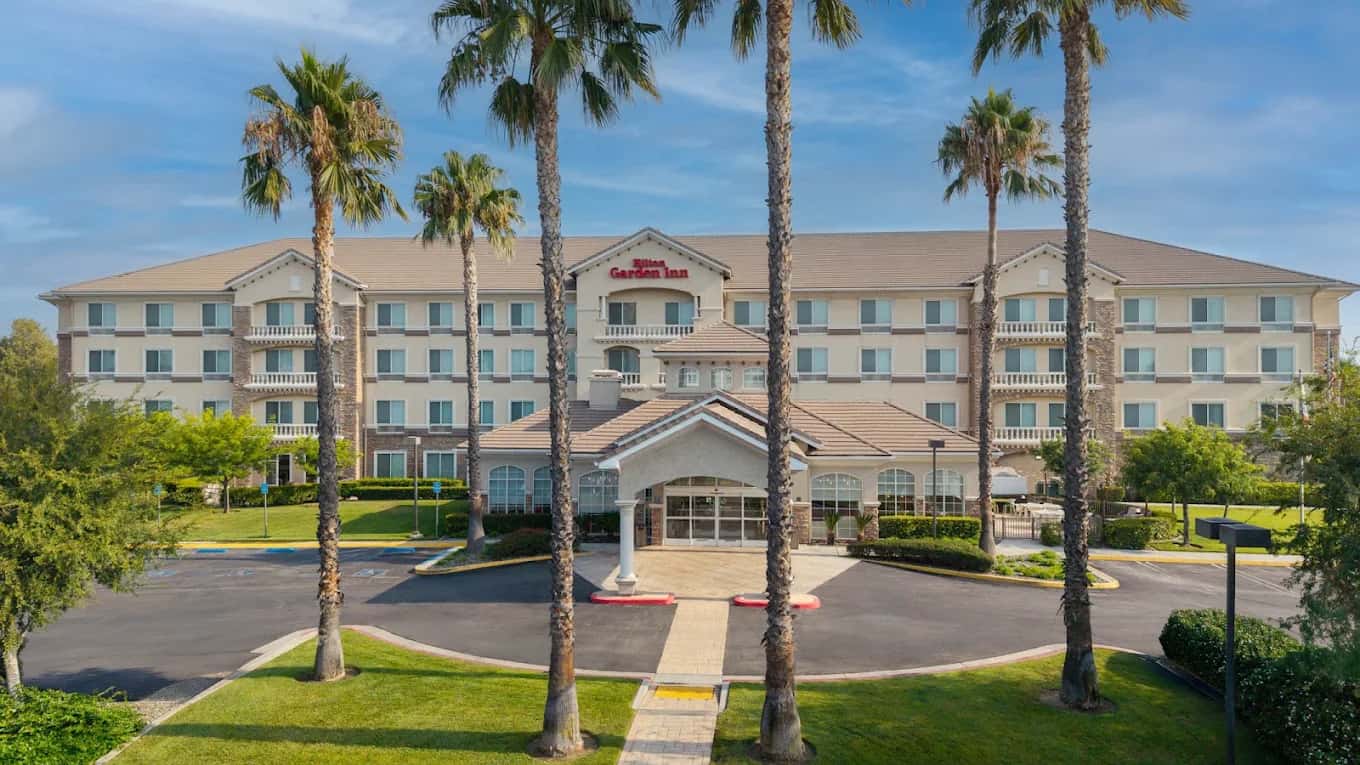 Palm-lined driveway and front entrance of the four-story Hilton Garden Inn Ontario/Rancho Cucamonga