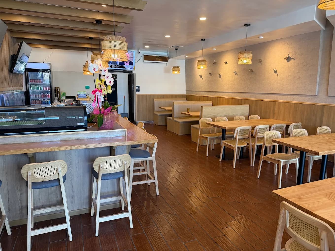 Dining room at Hinoki Men with a sushi counter, wooden tables, rattan chairs and pendant lamps