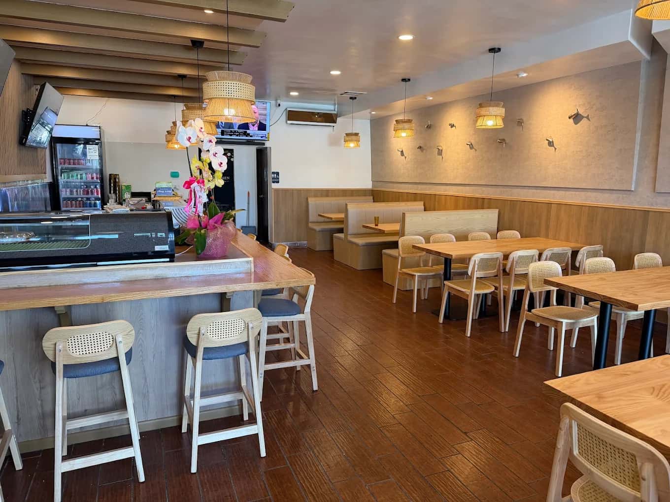Dining room at Hinoki Men with a sushi counter, wooden tables, rattan chairs and pendant lamps