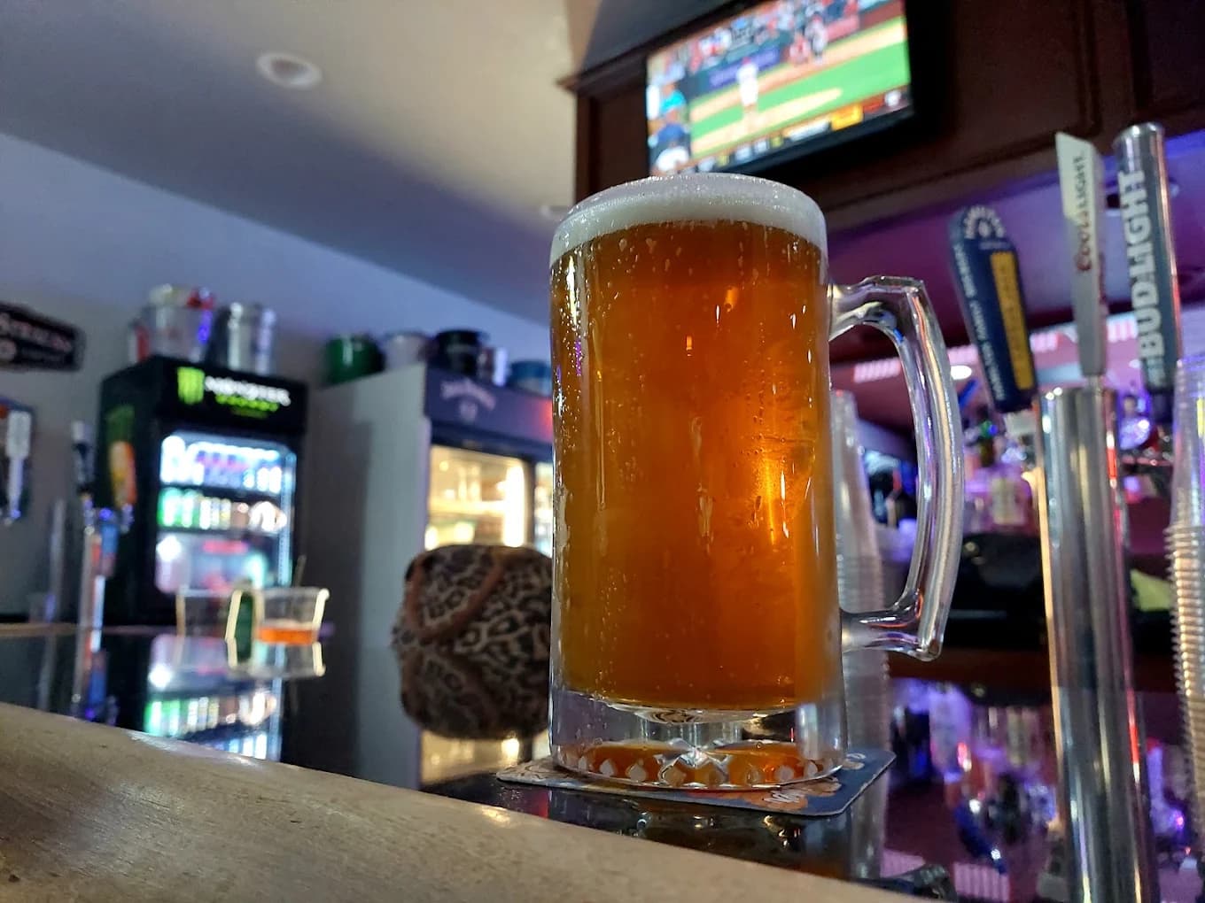 Frosty mug of beer on the bar at HK's Bar and Grill with taps and a TV showing baseball behind