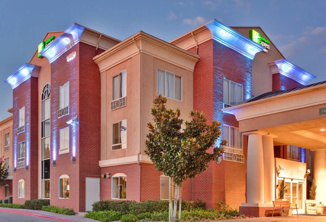 Red brick exterior of the Holiday Inn Express & Suites Ontario Airport-Mills Mall with blue-lit eaves at dusk