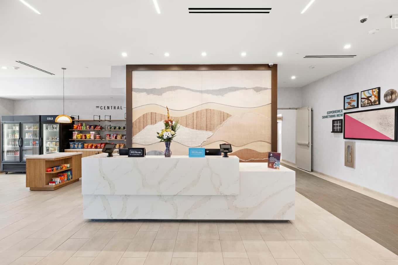 White marble front desk at the Home2 Suites by Hilton Ontario Airport, backed by layered landscape art and a snack shop