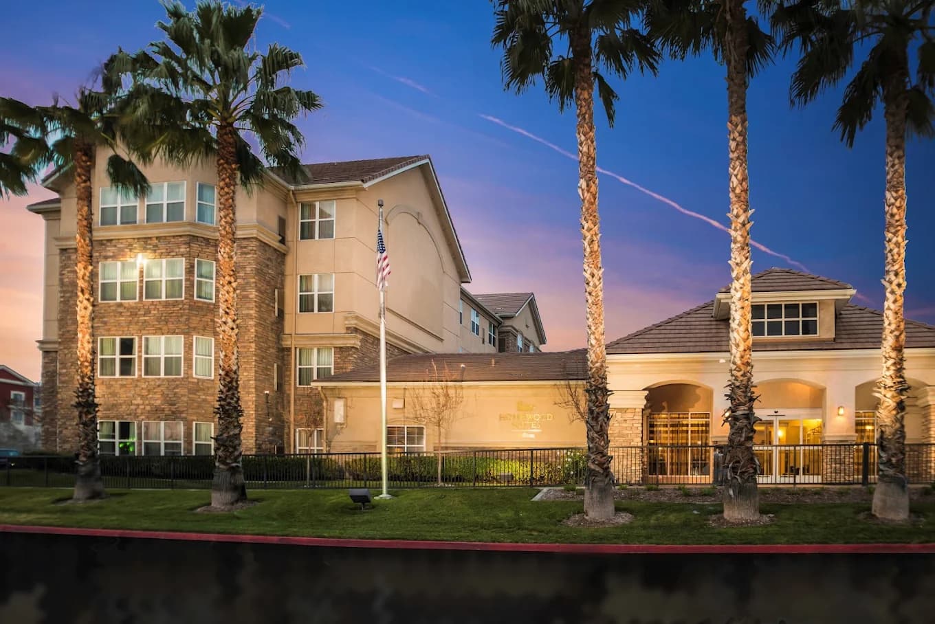 Palm trees and a flagpole in front of the Homewood Suites by Hilton Ontario-Rancho Cucamonga at sunset