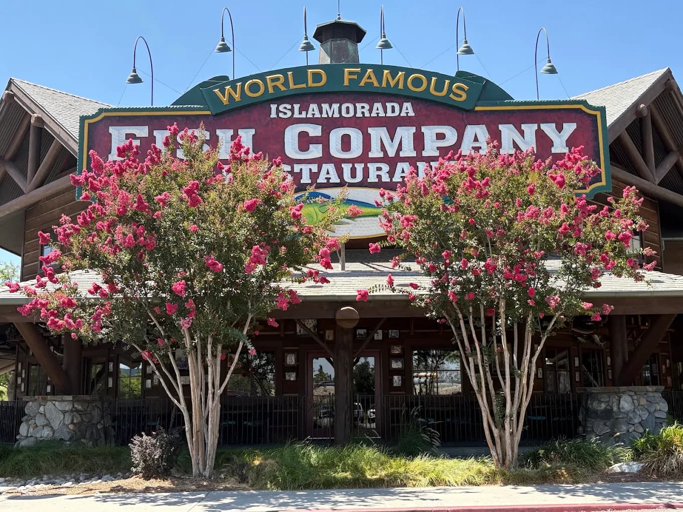 Wood-and-stone entrance and large World Famous Islamorada Fish Company sign framed by pink crape myrtles