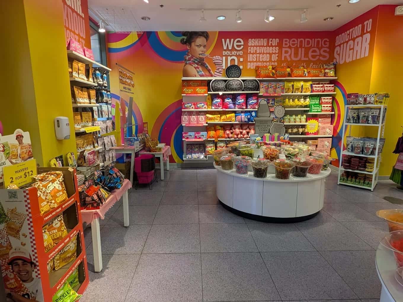 Inside IT'SUGAR, walls of sweets in yellow and pink around a round island of bulk candy bins