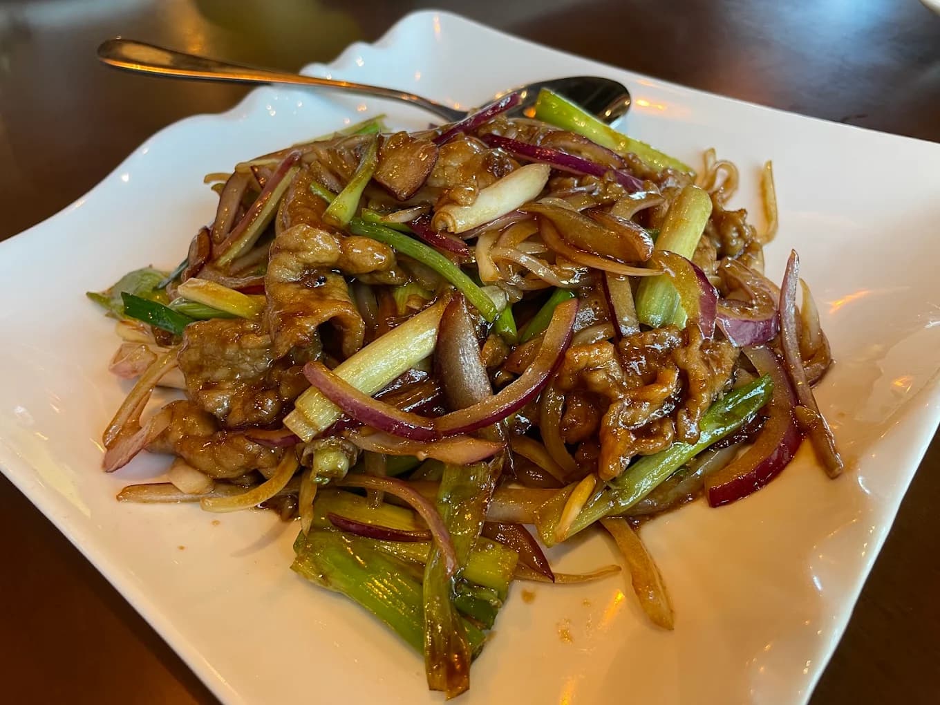 Stir-fried sliced beef with red onion and scallions on a square white plate at JJ Noodle House