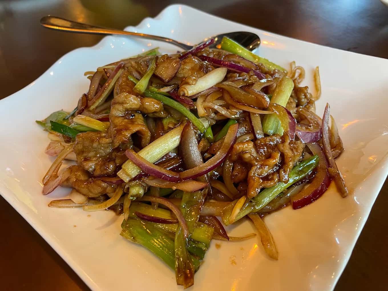 Stir-fried sliced beef with red onion and scallions on a square white plate at JJ Noodle House
