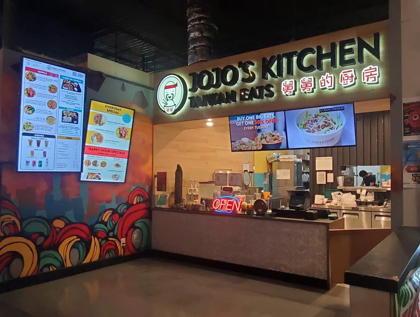 Counter, menu screens and neon Open sign at the Jojo's TaiwanEats food-hall stall with a colorful mural