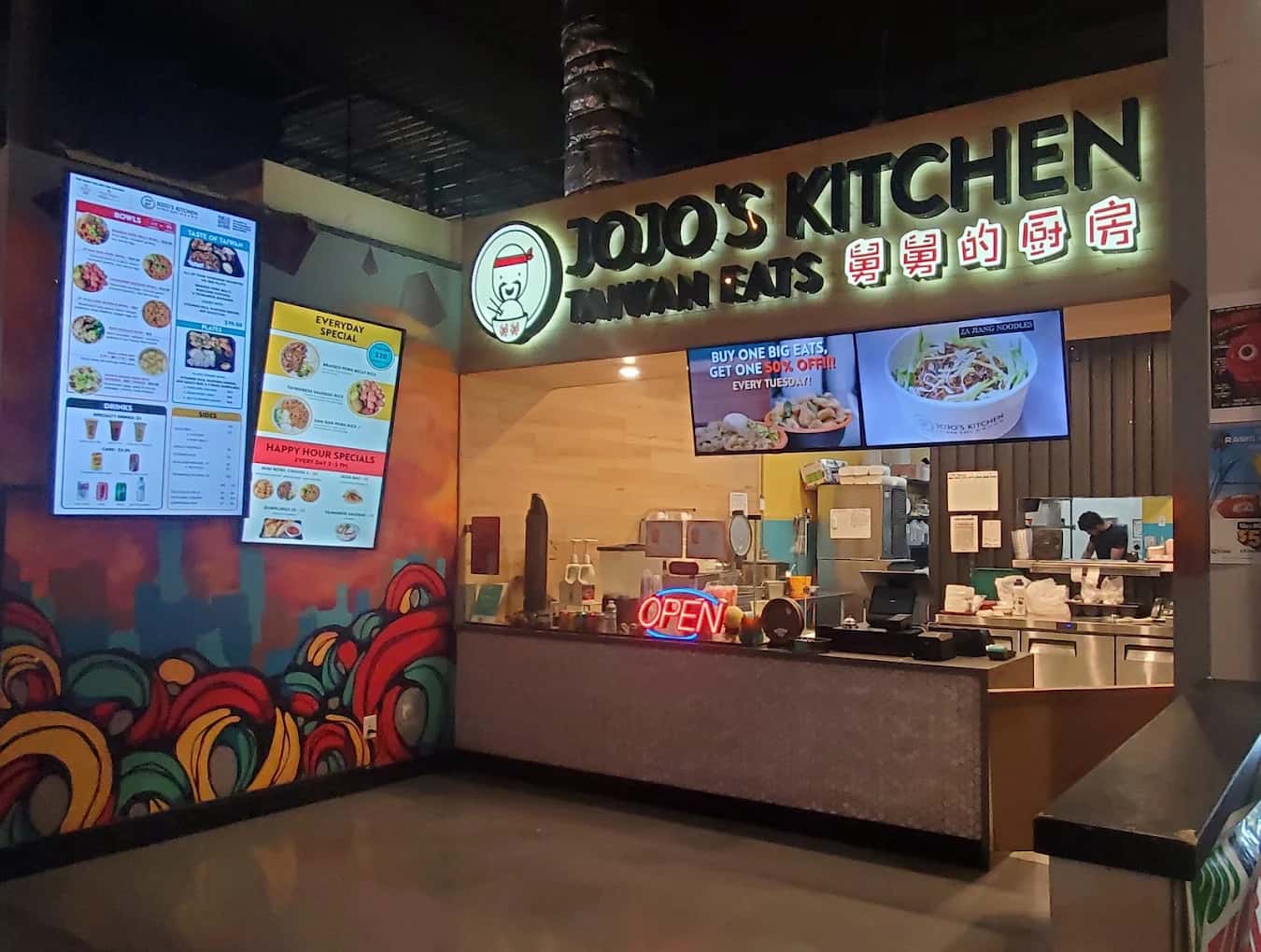 Counter, menu screens and neon Open sign at the Jojo's TaiwanEats food-hall stall with a colorful mural