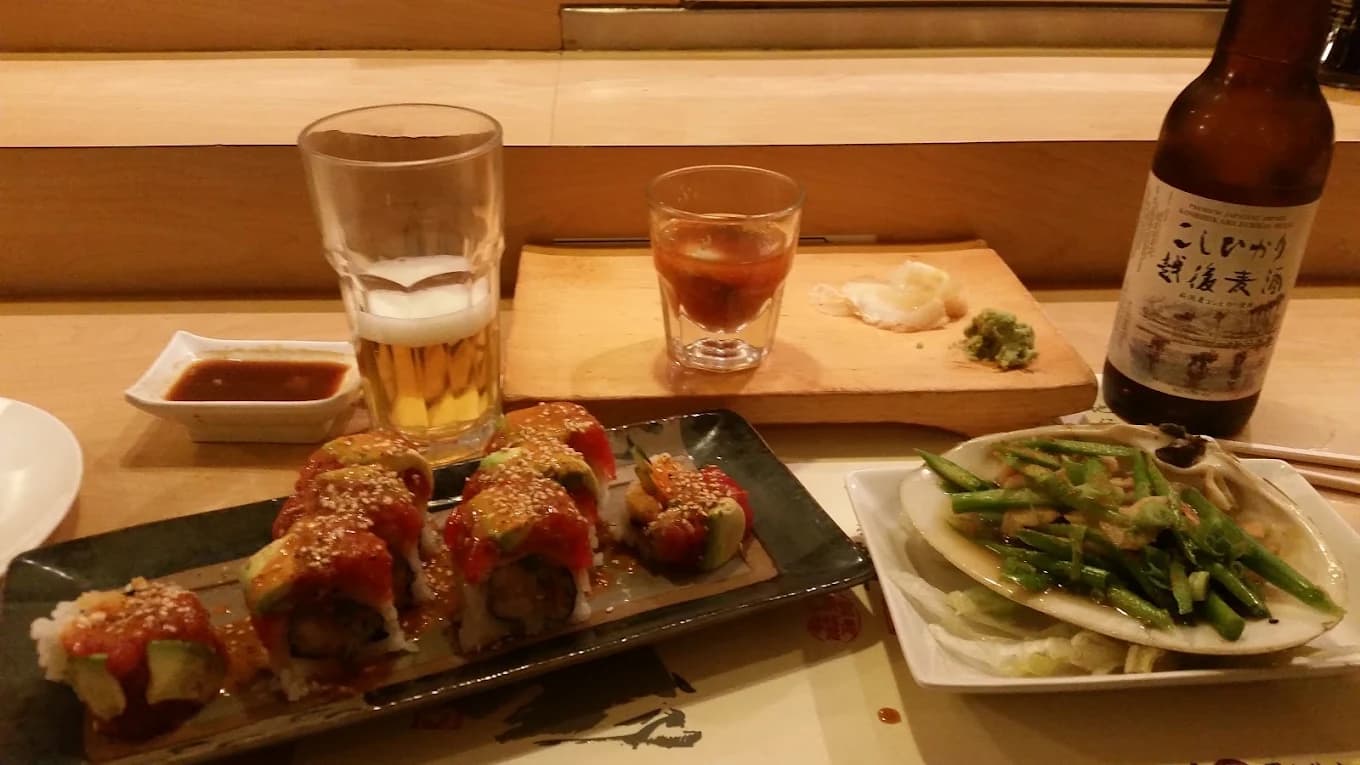 Sushi rolls topped with avocado, a plate of asparagus, beer and sake at the counter of Ken's Japanese Restaurant