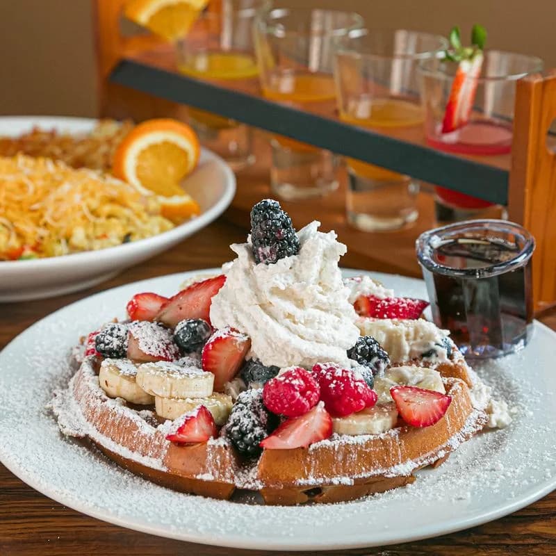 Waffle topped with berries, banana and whipped cream beside a mimosa flight at Kickback Jack's