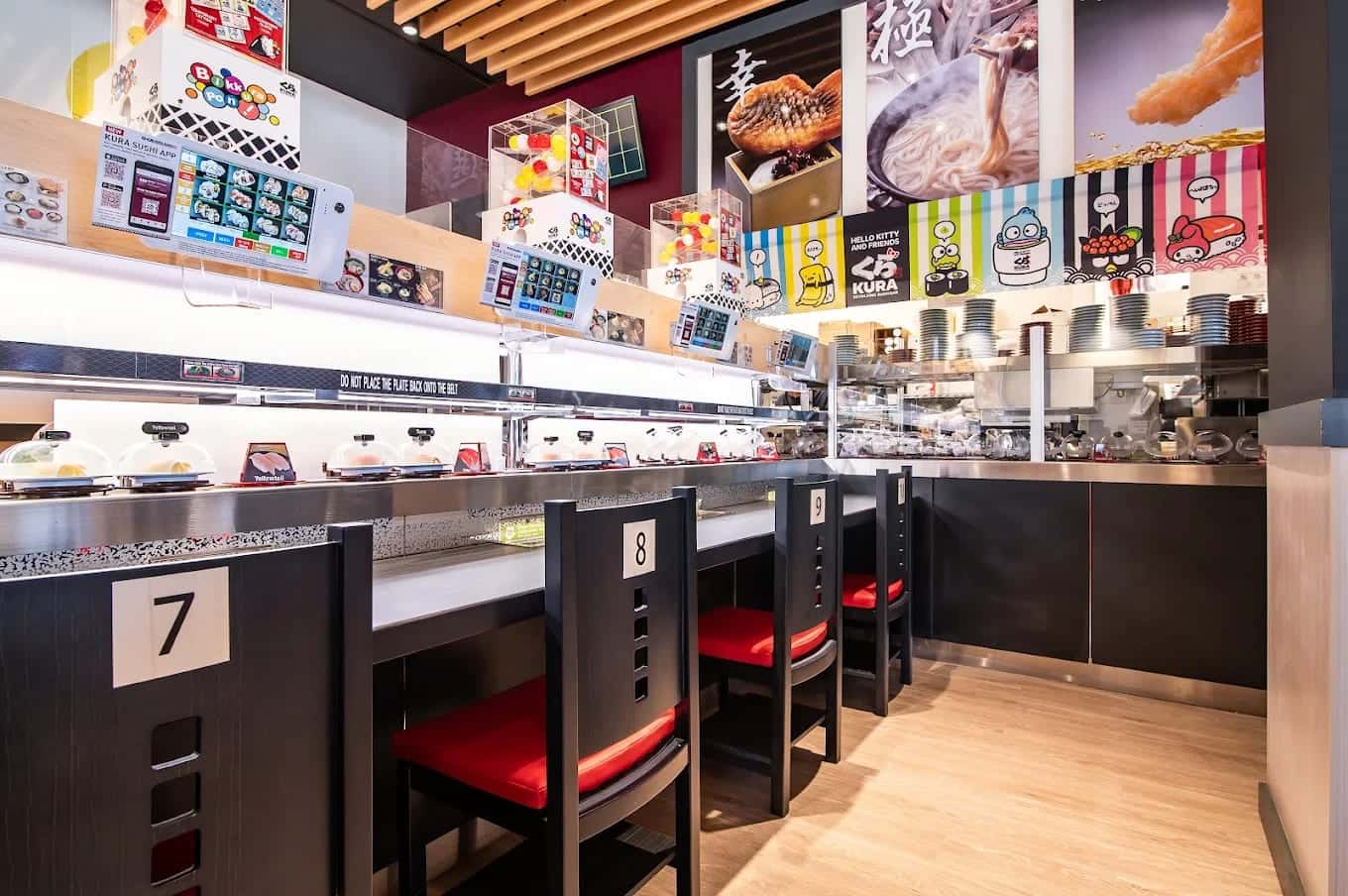 Numbered booths along the conveyor belt at Kura, covered sushi plates circling past red seats