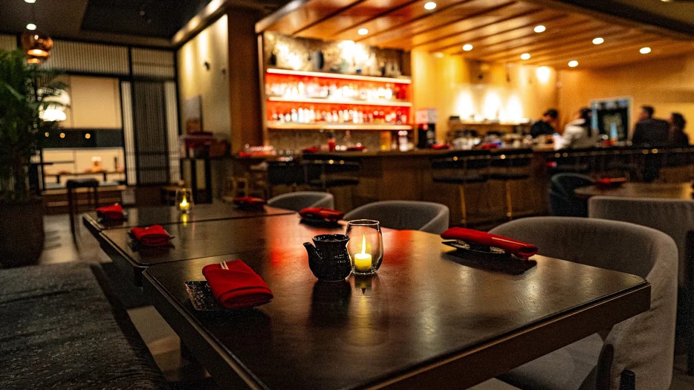 Dining room at KUWADA Sushi with candlelit tables, red napkins and a backlit bar