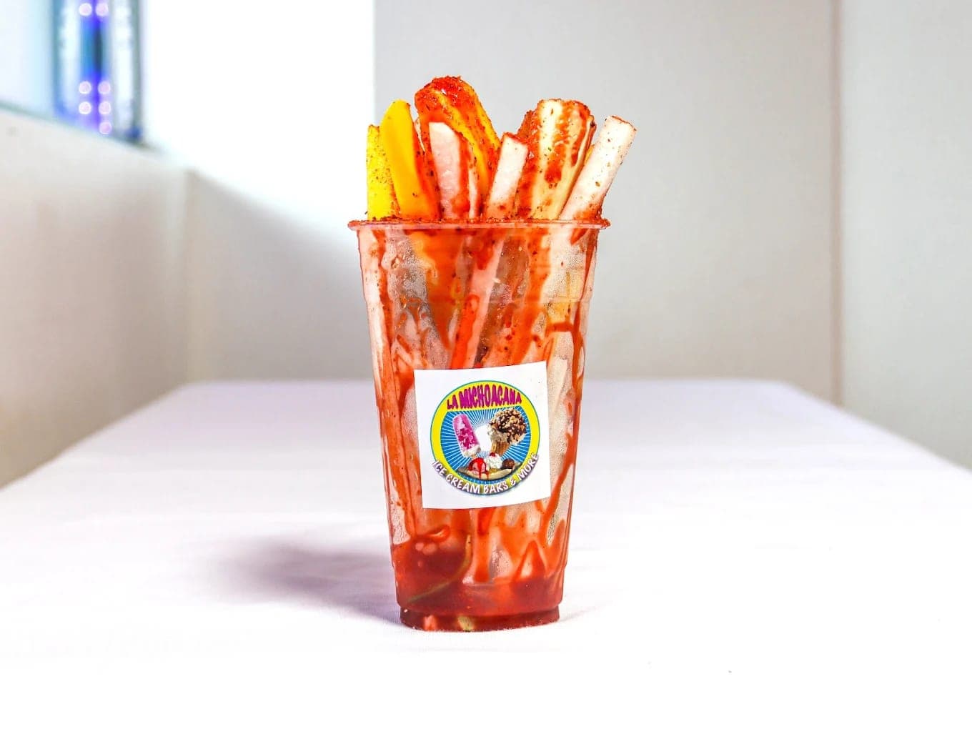 A tall cup of chamoy-covered fruit, mango and jicama spears dusted with chilli standing above the rim