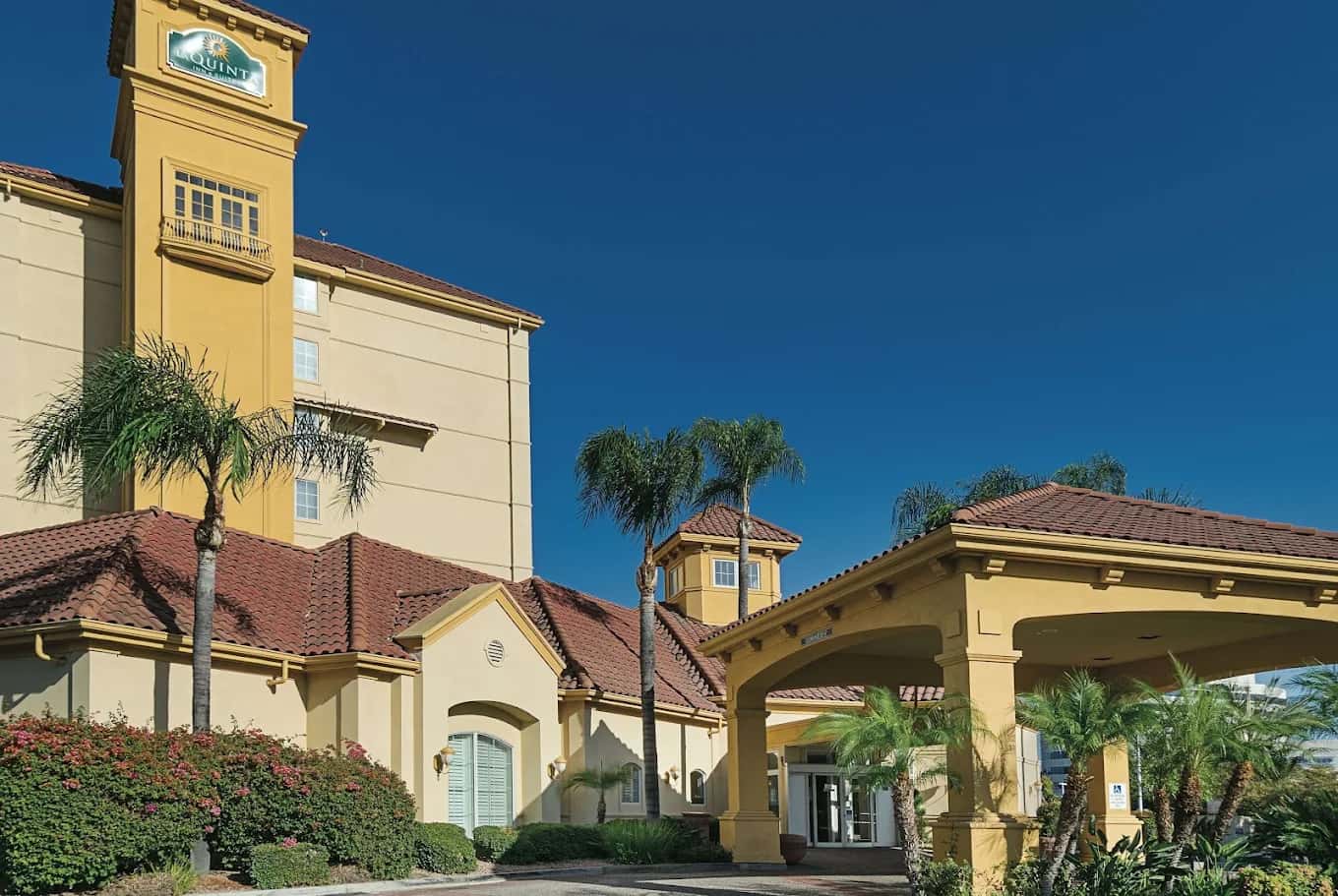 Yellow stucco La Quinta Inn & Suites exterior with red tile roofs, a covered entrance and palm trees under a blue sky