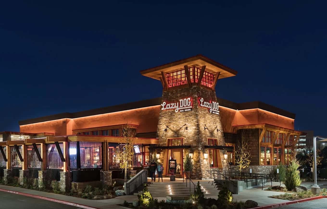 The Lazy Dog exterior at dusk, a stone-and-timber lodge front lit warmly under a deep blue sky