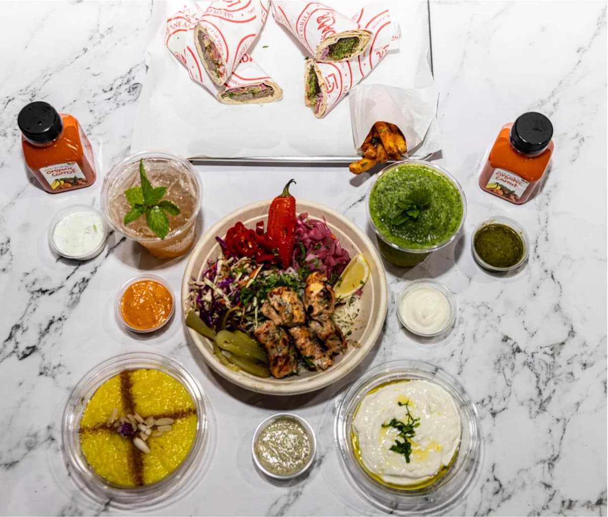 Overhead spread of chicken kebab bowl, wraps, rice, dips and drinks from Lidaar Mediterranean Grill