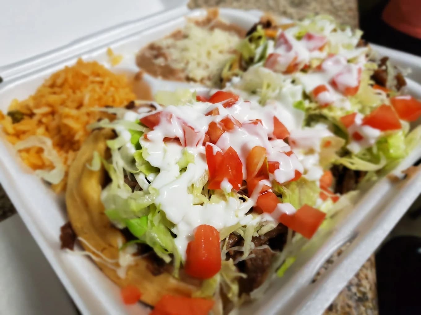 Takeout tray of sopes topped with lettuce, tomato and crema with rice and beans from Los Jalapeños Jr Inc