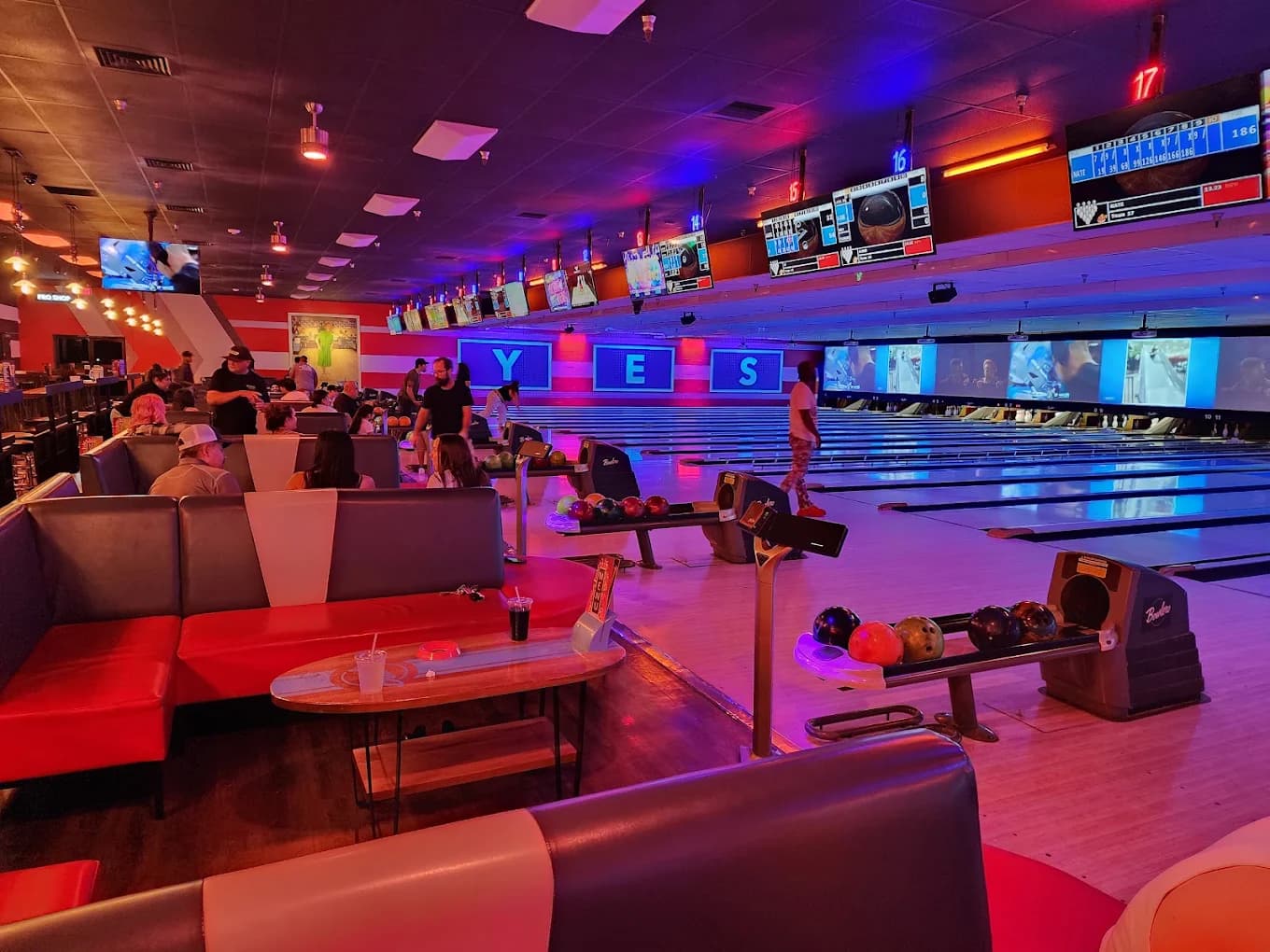 Bowling lanes, ball returns and booth seating under colored lights at Lucky Strike