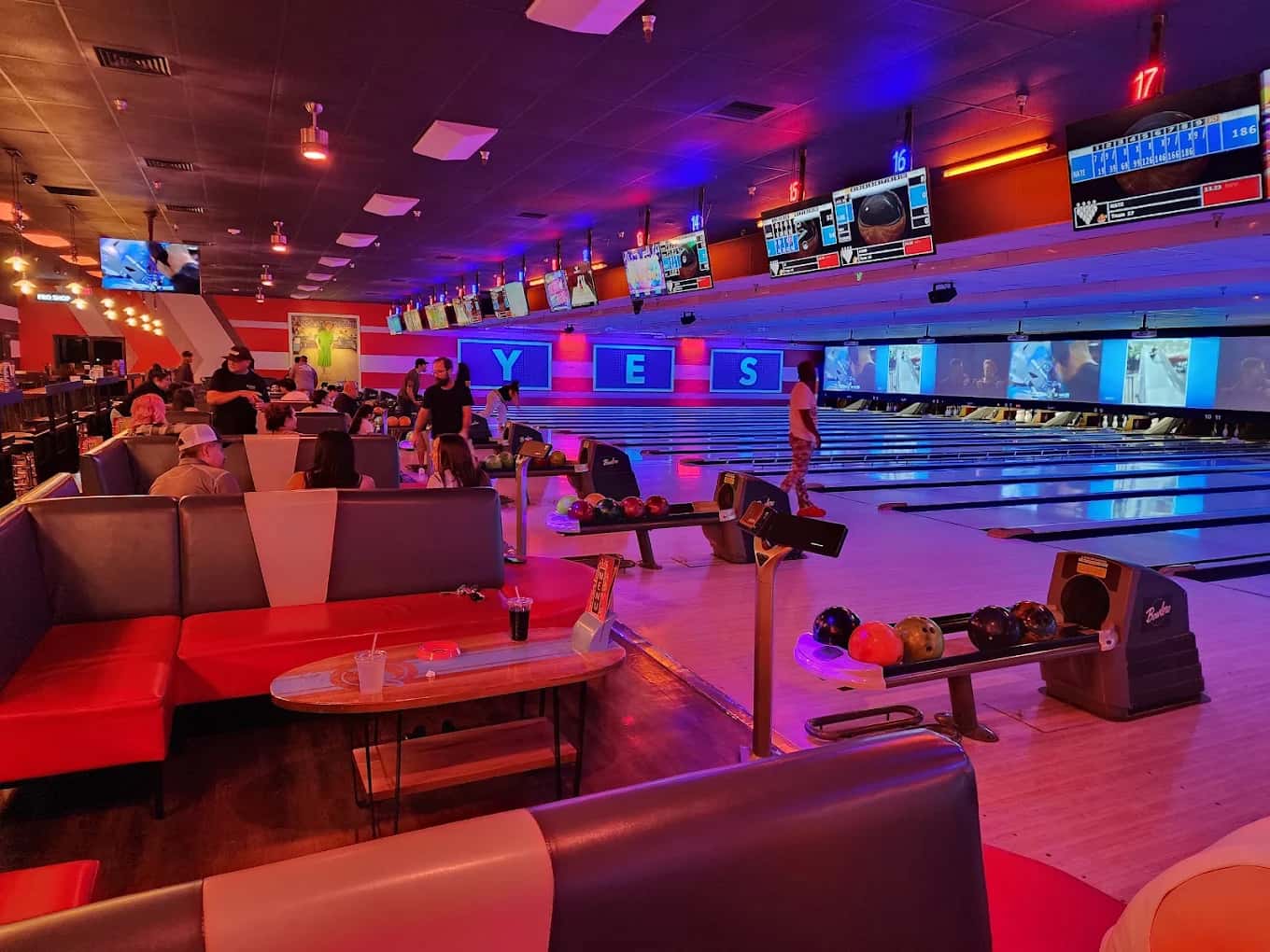 Bowling lanes, ball returns and booth seating under colored lights at Lucky Strike