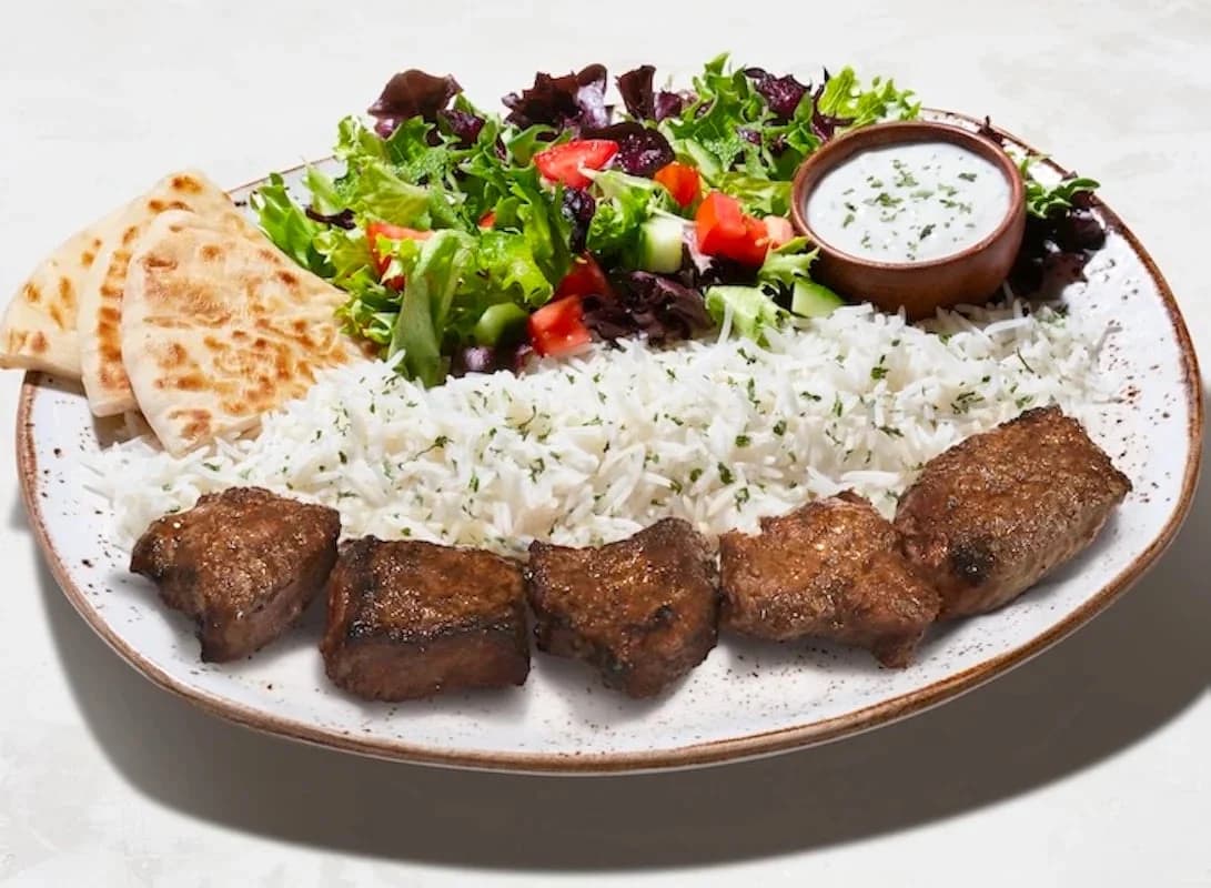Luna Grill platter of grilled beef pieces over herbed rice with pita wedges, a green salad and a cup of white sauce