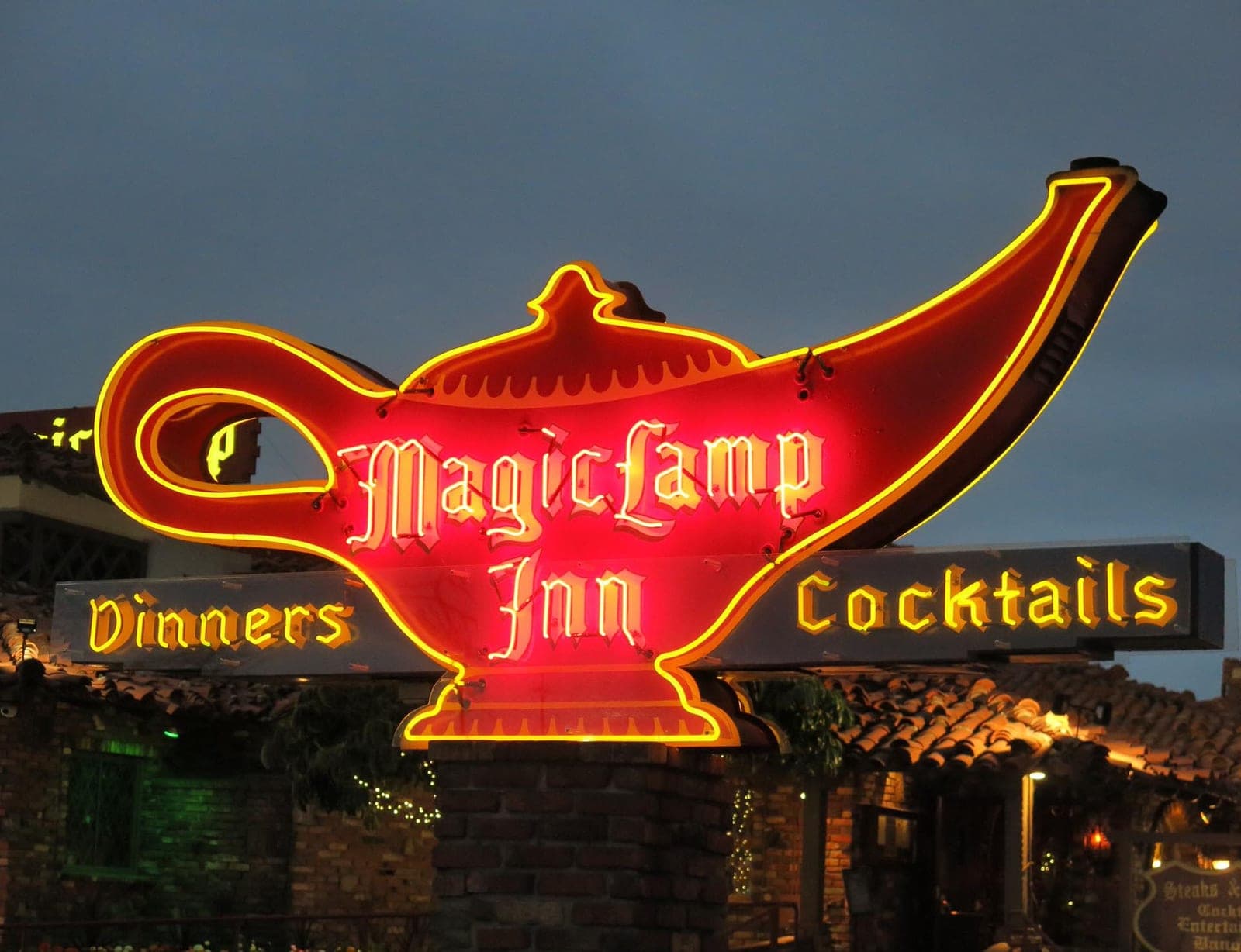 The Magic Lamp Inn neon sign at dusk, a red and gold genie lamp glowing above the words Dinners and Cocktails