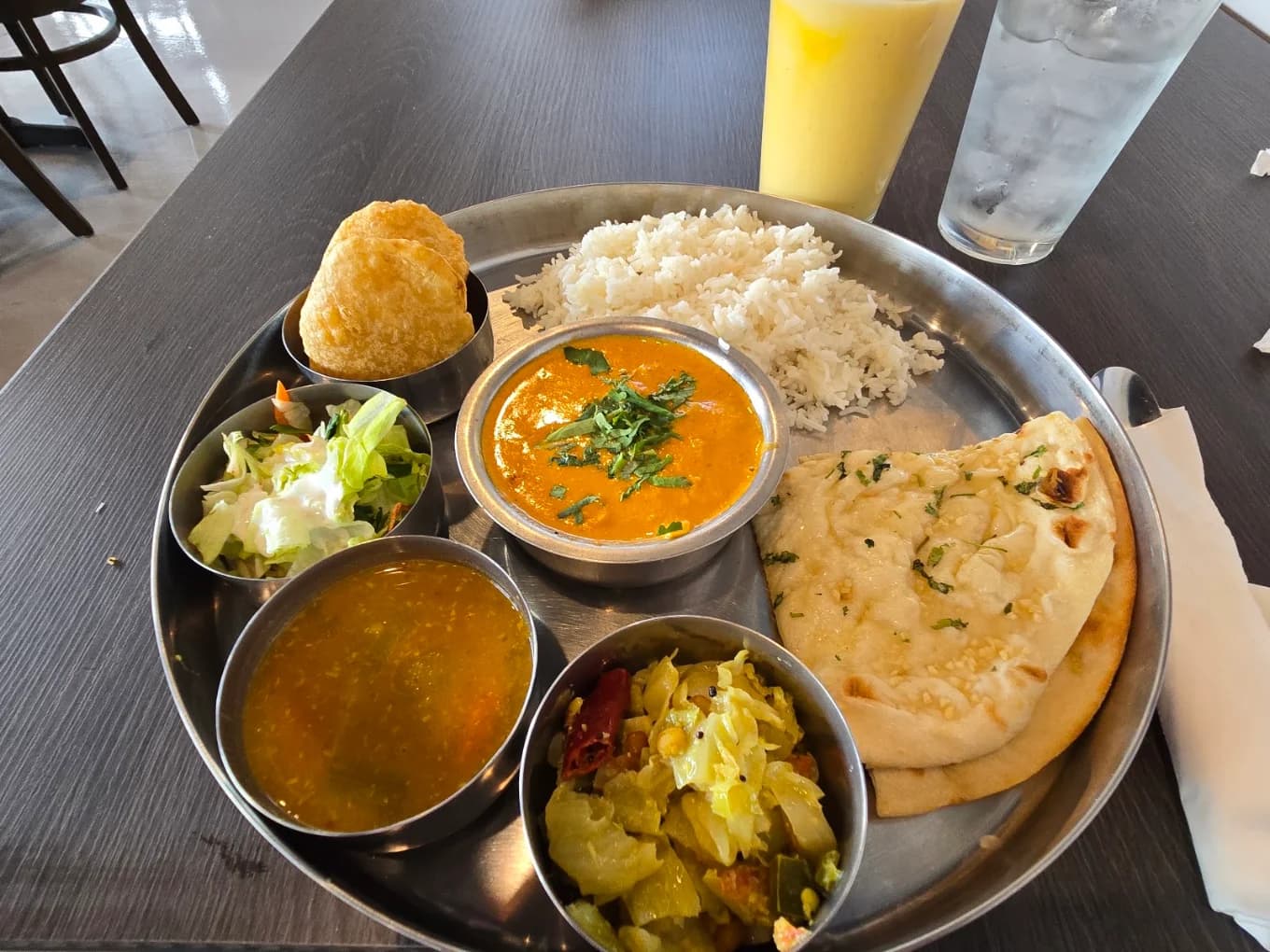 Steel thali tray with curry, dal, rice, naan, poori and salad at Maharaja Kitchen
