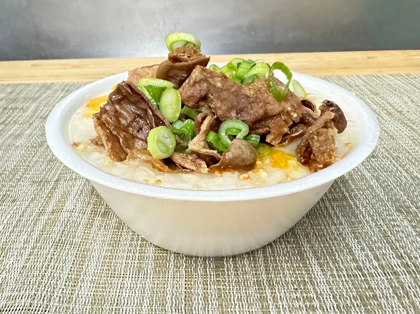 Bowl of rice porridge topped with fried meat and sliced green onions from Manila Sunset Grille