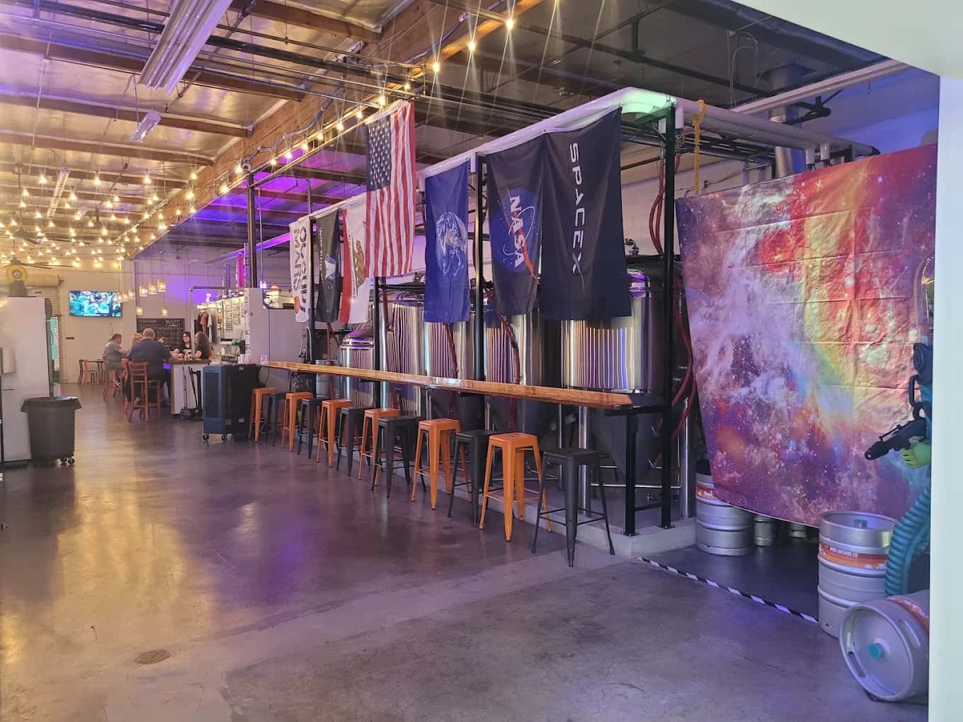 Taproom at Mars Brewing Company with bar stools, steel fermenting tanks and NASA and SpaceX flags