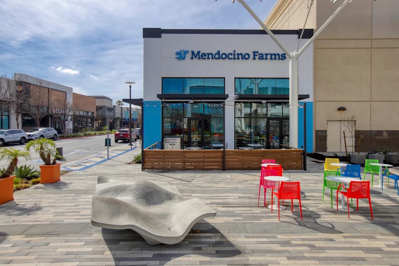 Storefront of Mendocino Farms with a fenced patio and colorful plastic chairs on a plaza