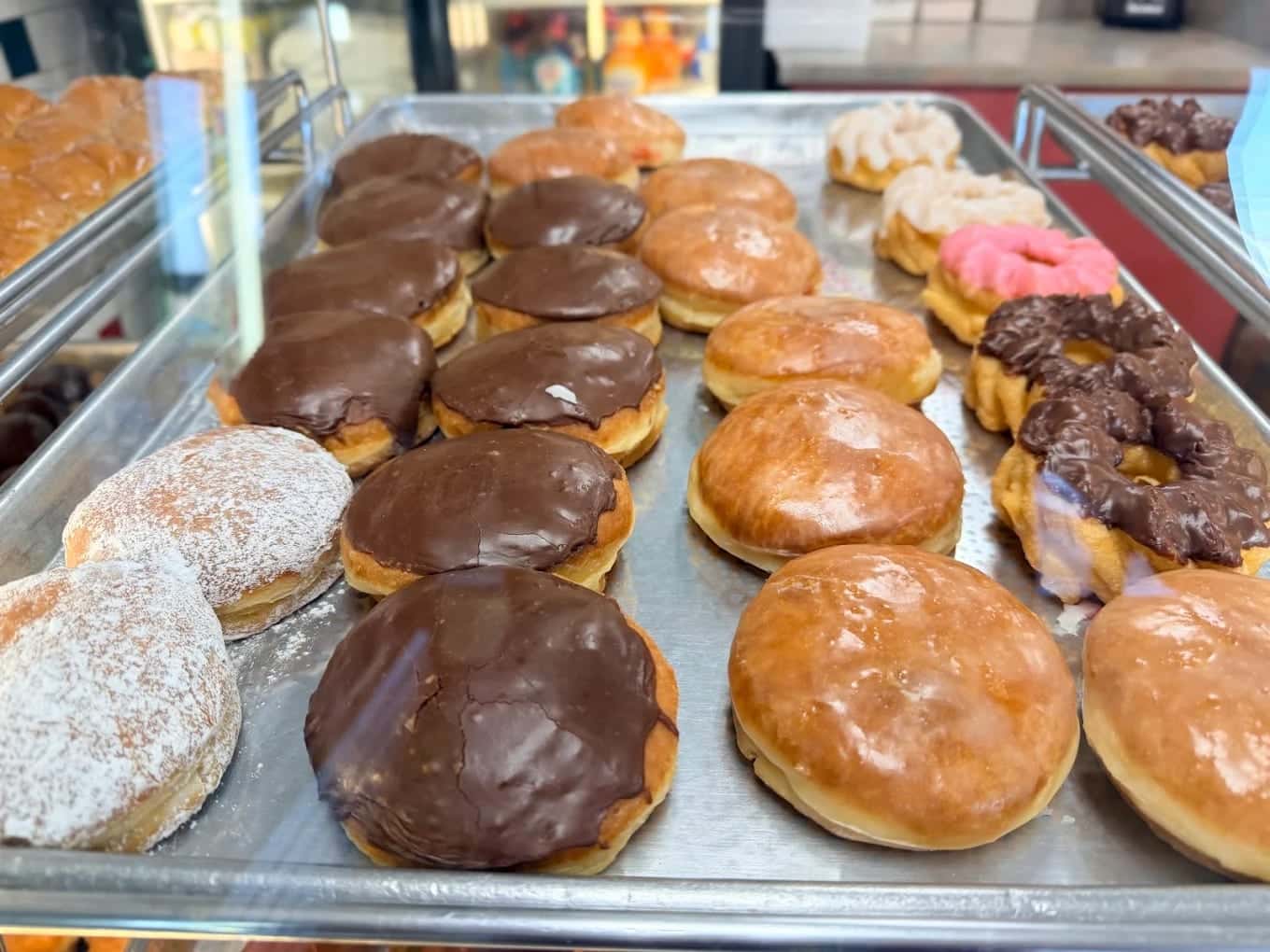 A bakery tray of donuts: chocolate-topped bars, glazed rings, sugar-dusted rounds and a pink-iced twist