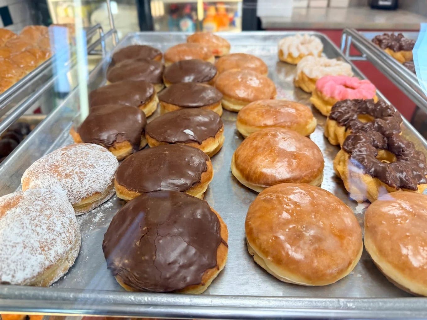 A bakery tray of donuts: chocolate-topped bars, glazed rings, sugar-dusted rounds and a pink-iced twist