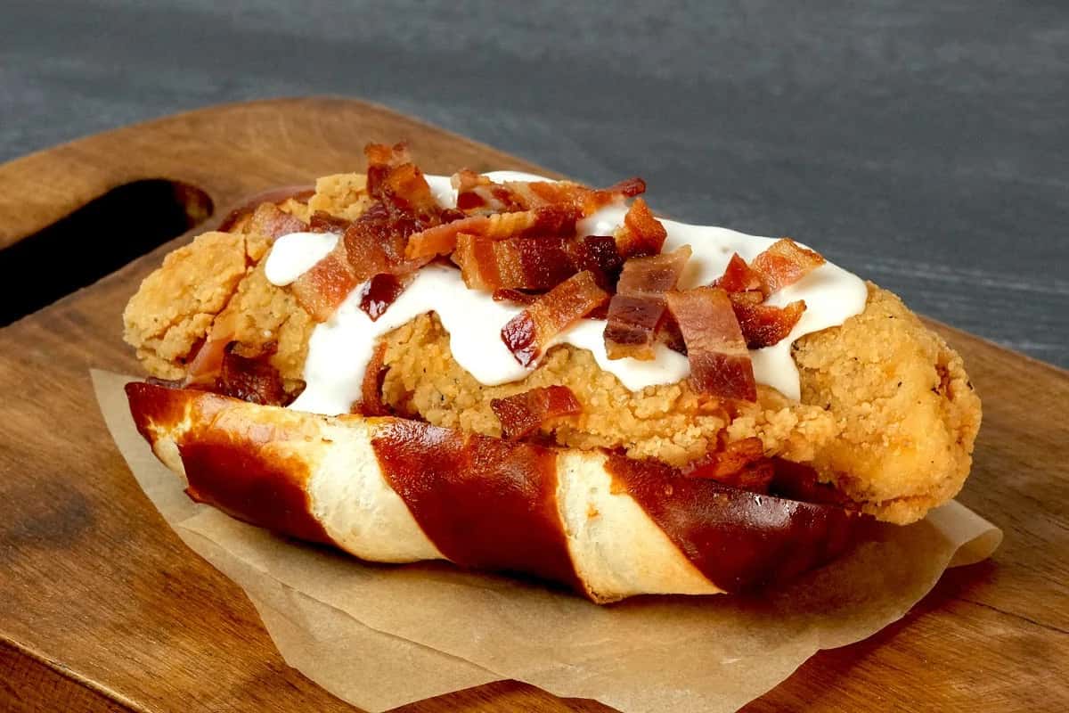 Fried chicken in a pretzel bun topped with white sauce and bacon pieces from MLB Ballpark Bites