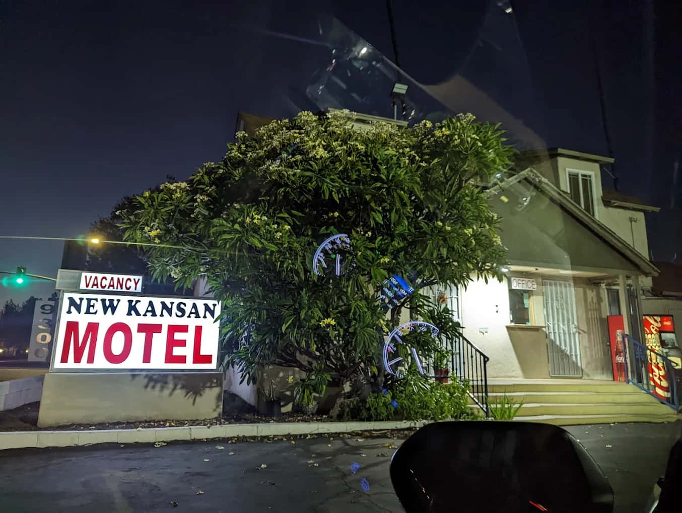Lit vacancy sign and office entrance at New Kansan Motel at night, tree in front