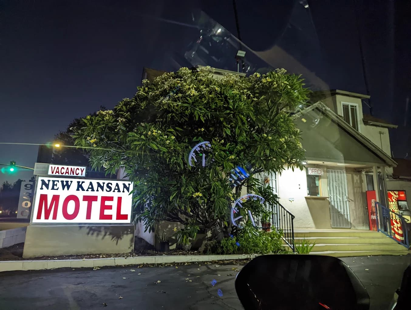 Lit vacancy sign and office entrance at New Kansan Motel at night, tree in front