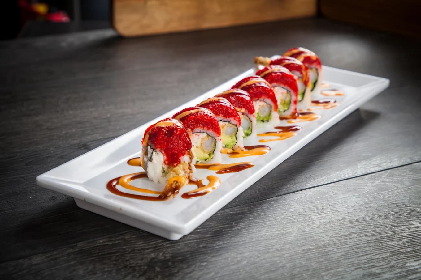 Sushi roll topped with red tobiko and drizzled sauces on a long white plate at Ozen