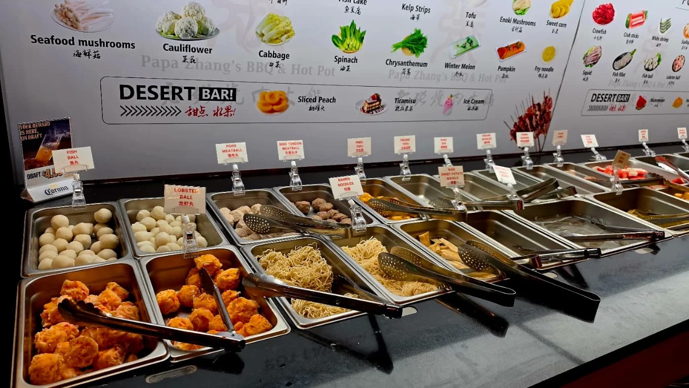 Hot pot ingredient bar at Papa Zhang’s BBQ & Hot Pot with labeled trays of meatballs, noodles and tofu