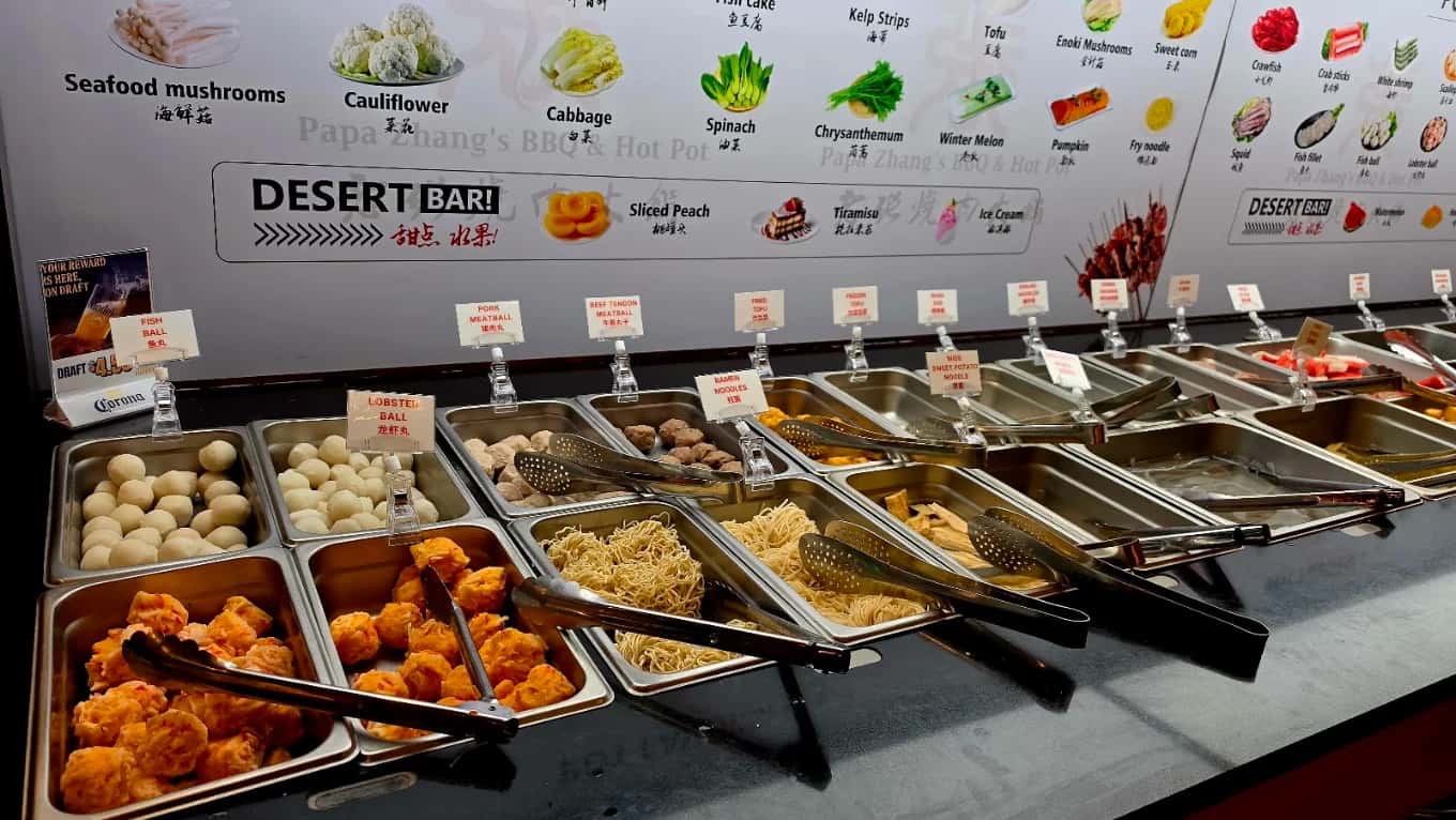 Hot pot ingredient bar at Papa Zhang’s BBQ & Hot Pot with labeled trays of meatballs, noodles and tofu