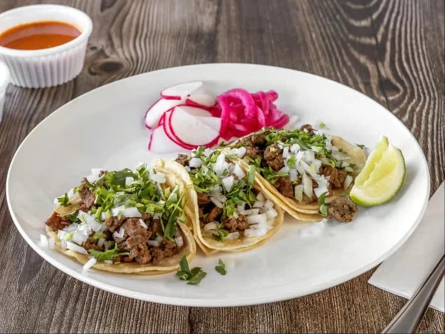 Three street tacos with onion, cilantro, radish and lime on a plate at Pepe's Finest Mexican Food