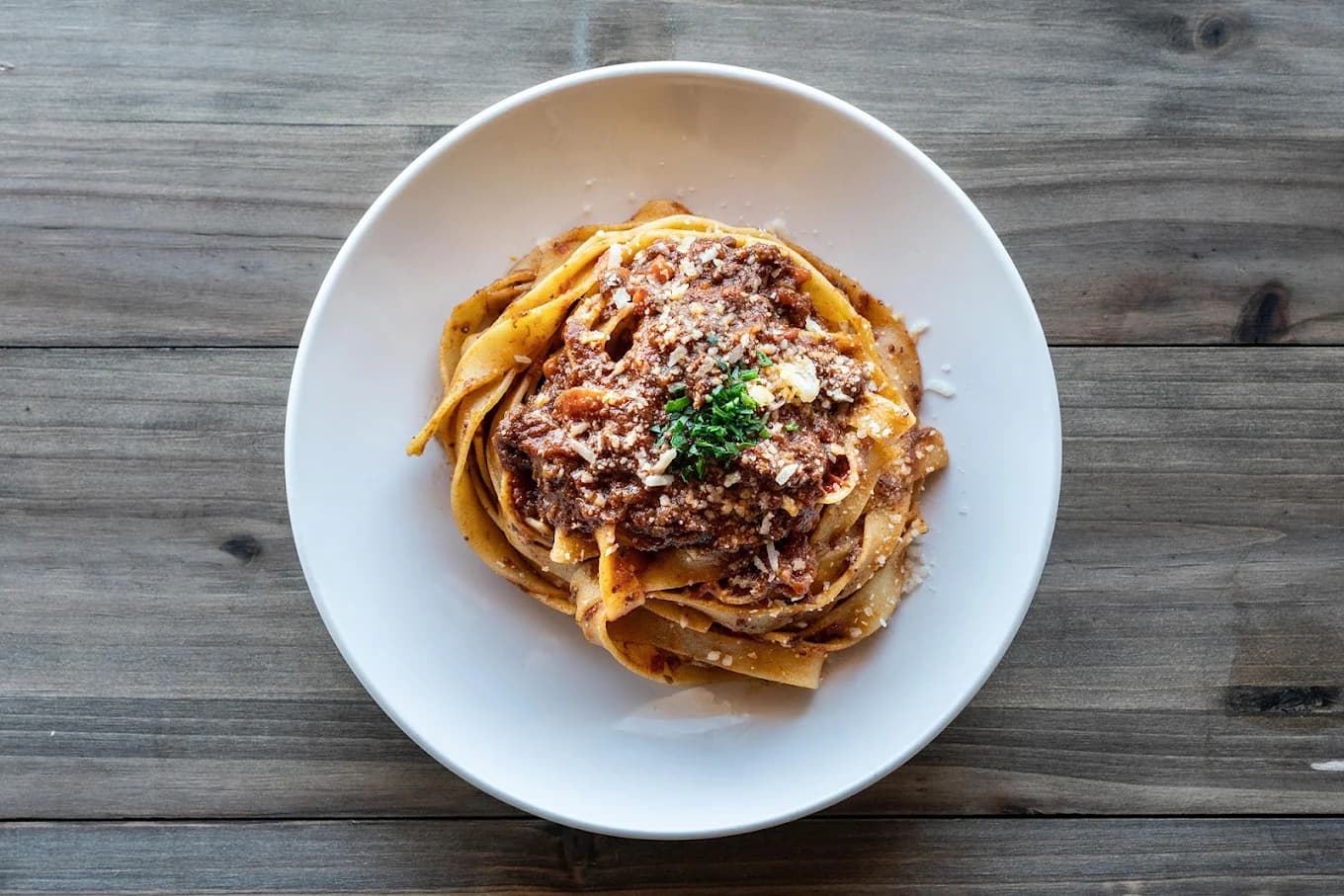Overhead view of tagliatelle topped with meat ragu, grated cheese and parsley at Pinwheel Pasta