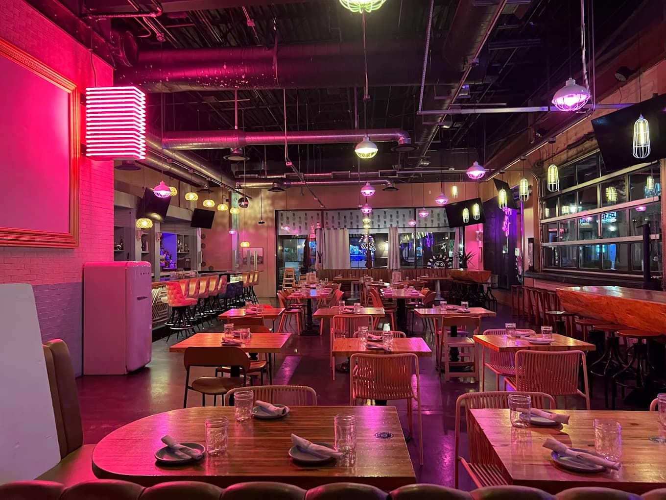 Dining room at Punch Bowl Social with wood tables, pink neon lighting and a bar in the background
