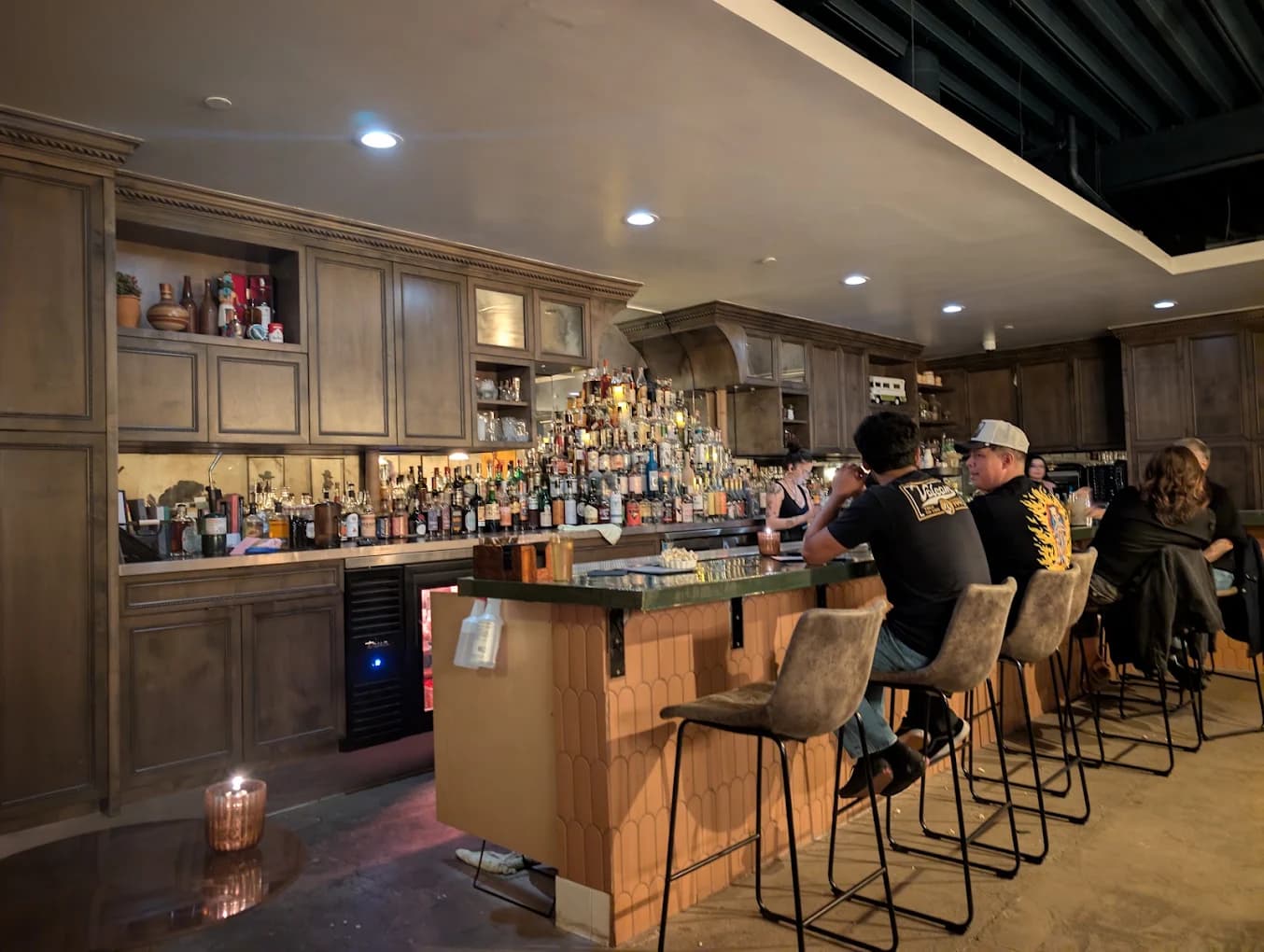 Guests seated at the bar at Raffael’s Silver Cloud Lounge Club with a wall of liquor bottles behind