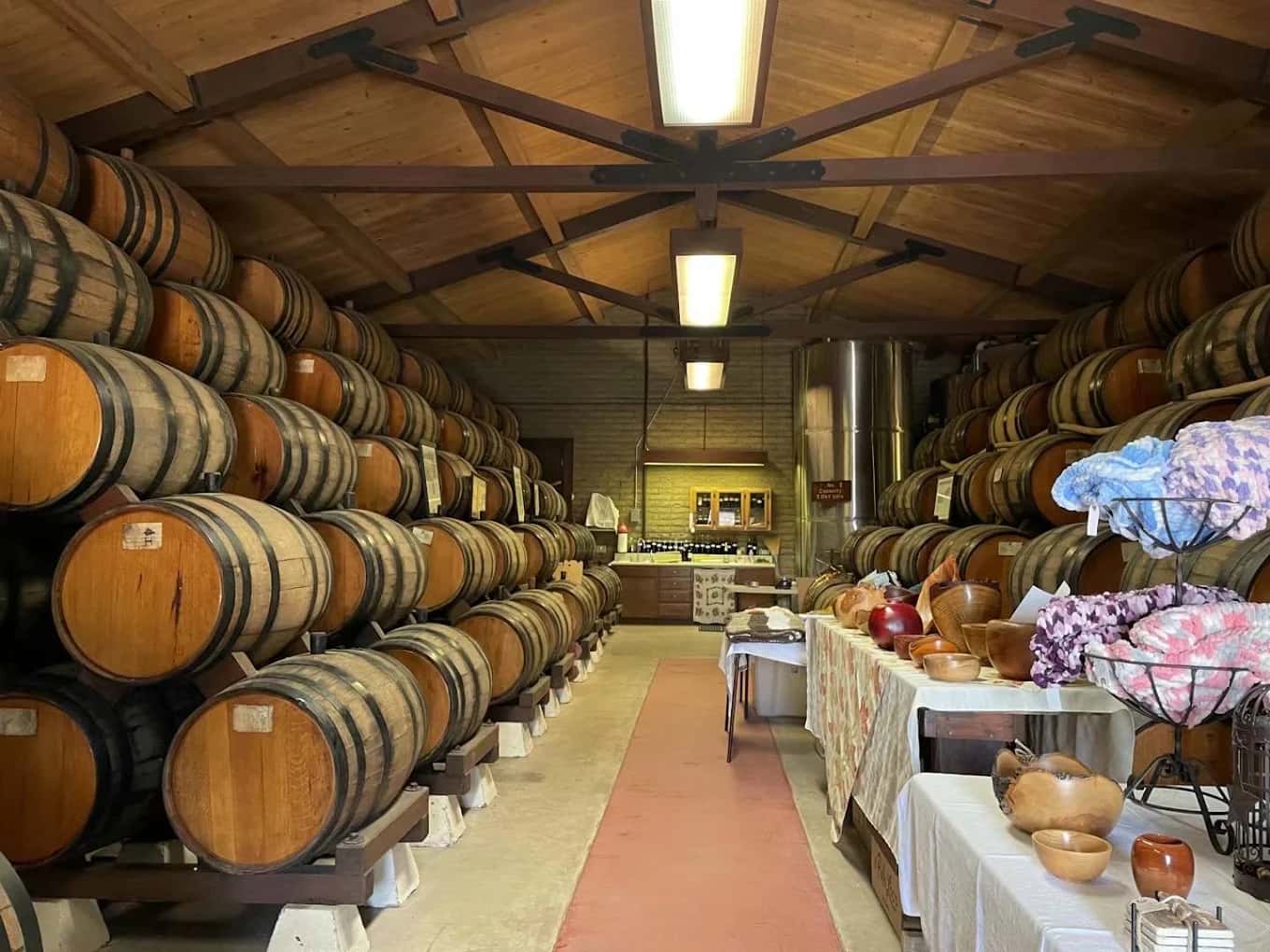 Stacked oak barrels lining the barrel room at Rancho de Philo Winery, with a table of wooden bowls