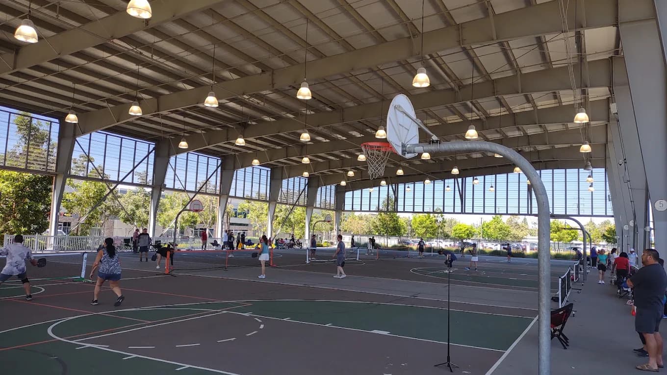 Covered outdoor courts at RC Sports Center with people playing pickleball under basketball hoops