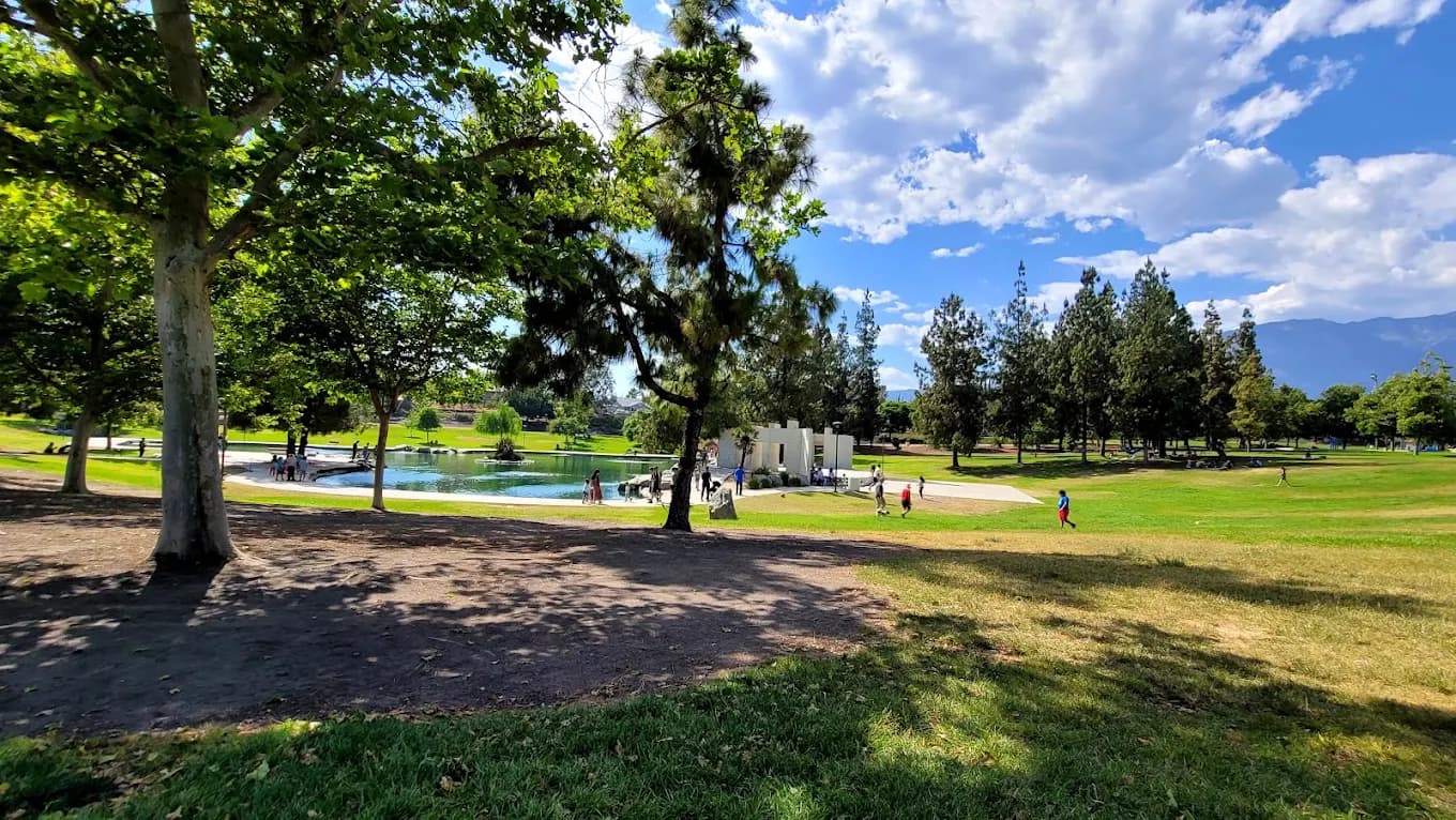 Grass lawn, shade trees and a pond at Red Hill Community Park with mountains in the distance
