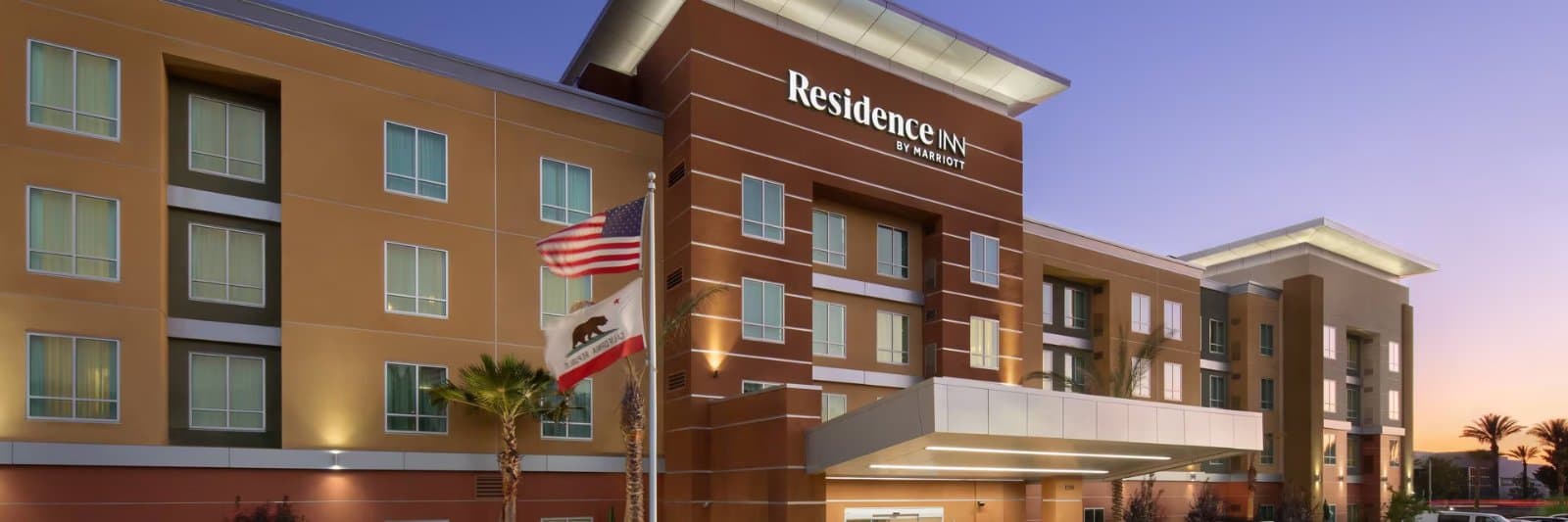 Residence Inn by Marriott's brown and tan hotel exterior at dusk with US and California flags flying by the entrance