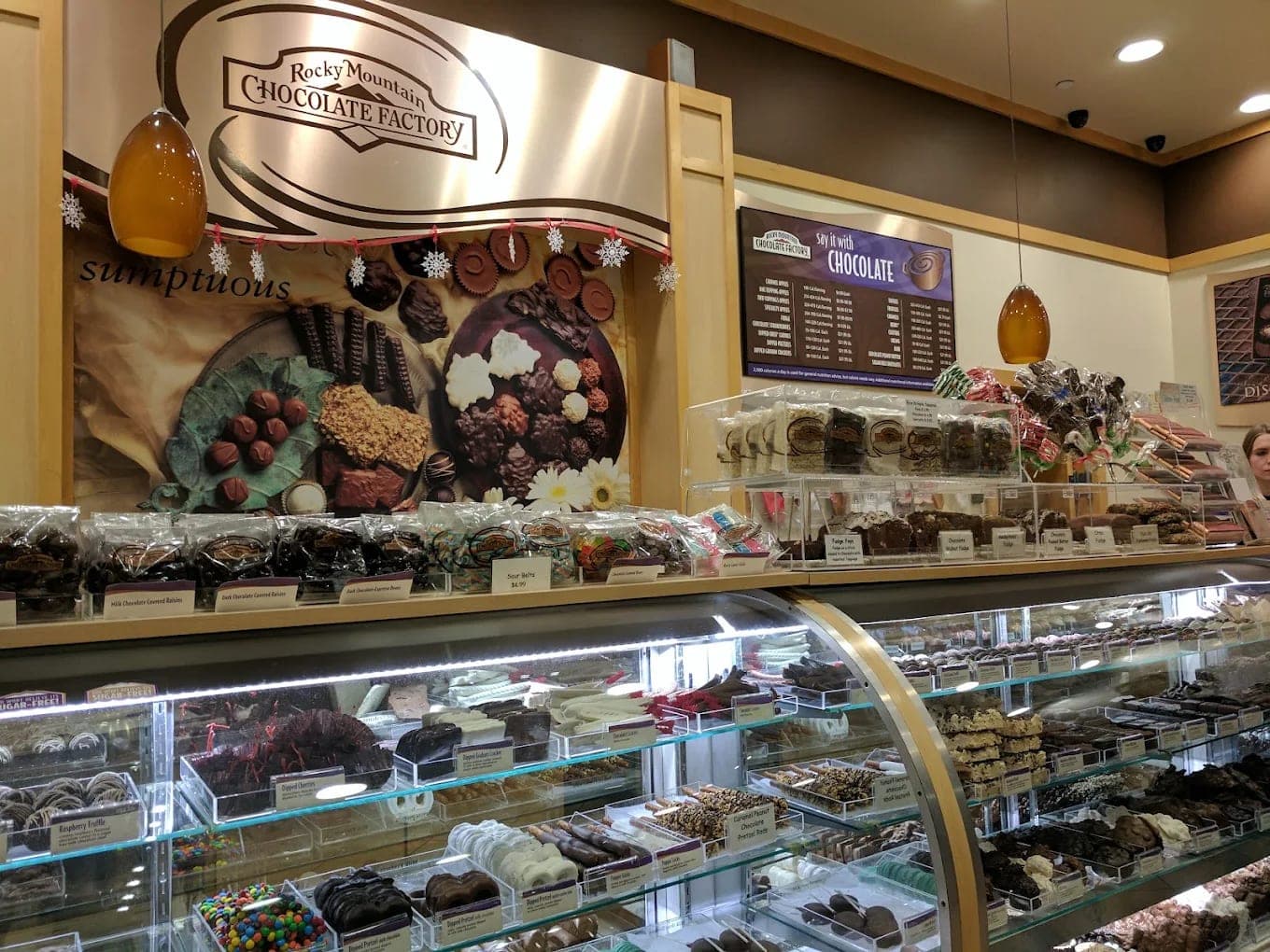 A chocolate shop counter, glass cases of truffles and dipped fruit below a wall of bagged confections