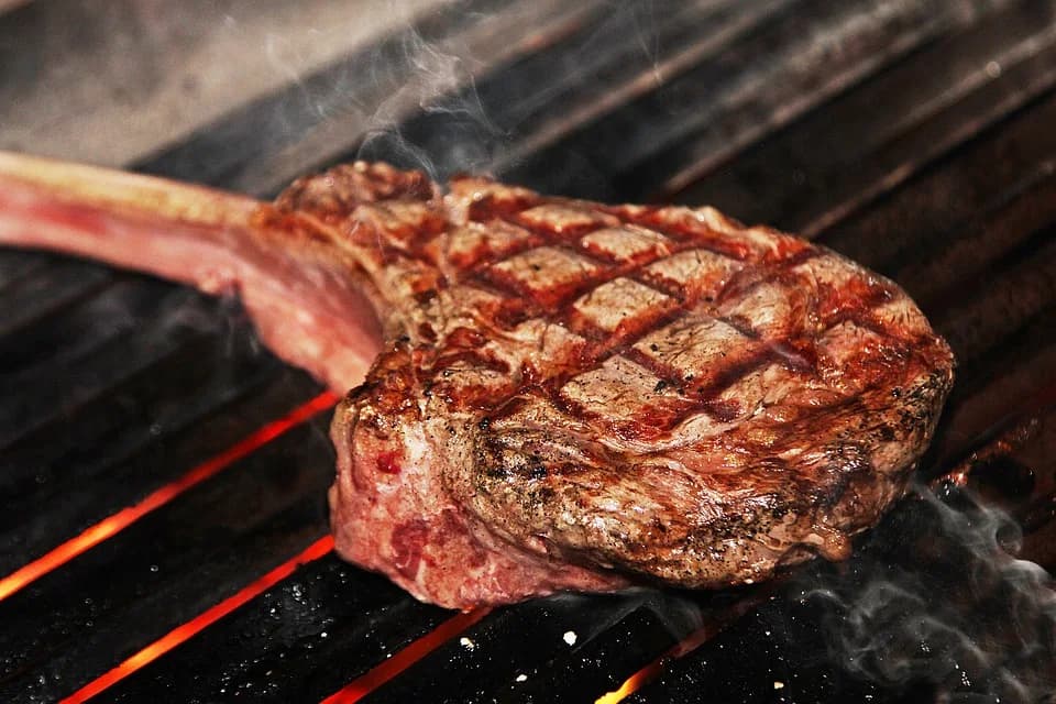A bone-in steak with crosshatch grill marks searing over glowing coals at Rodeo Café