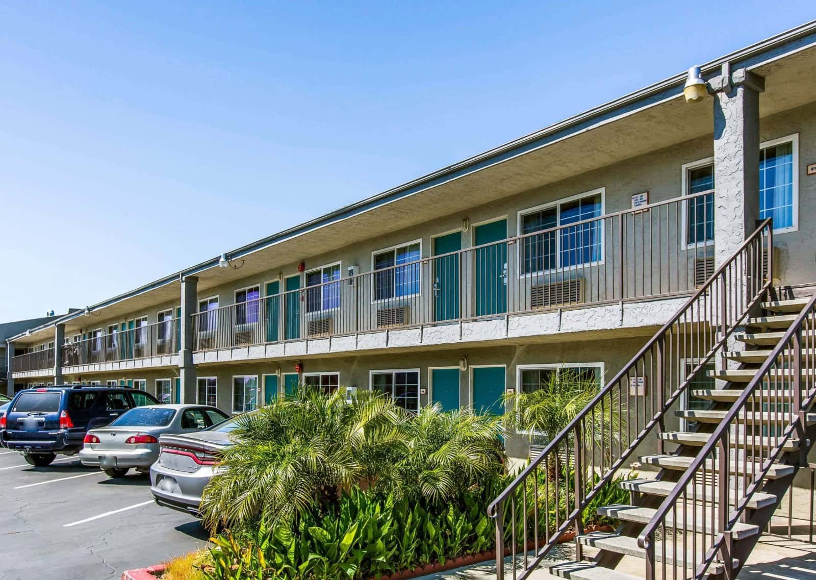 Two-story Rodeway Inn motel building with teal doors, exterior walkway railings and a stairway beside the parking lot